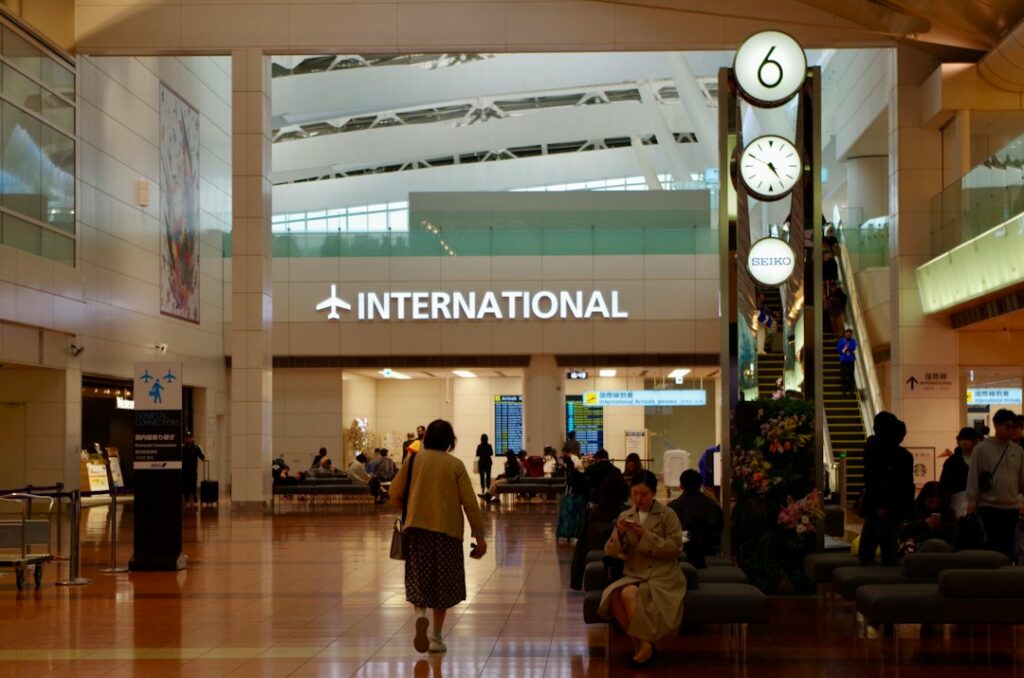 Generic airport terminal hall with clocks for city-origin versus airport-origin scope; illustrative stock photograph, not TransferHub fleet or an actual pickup point